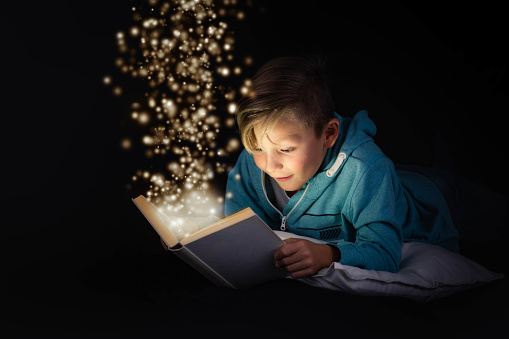 blond boy reading a magicical story book with light leaping off the page